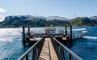 Houten steiger naar veerpontdok op blauw meer in Jotunheimen. Besneeuwde bergen op achtergrond onder gedeeltelijk bewolkte hemel.