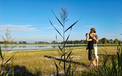 Stel staat samen en kijkt door hoog riet naar de Neusiedlersee. Het meer strekt zich uit op de achtergrond onder een blauwe lucht met witte wolken.