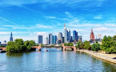 Frankfurt am Main skyline met moderne wolkenkrabbers en historische gebouwen langs de Main onder blauwe hemel met witte wolken.