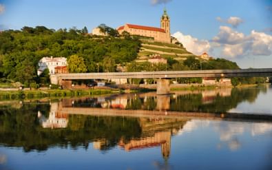 Kasteel Mělník met zijn kenmerkende toren staat op een heuvel boven de Elbe. Een moderne brug overspant het water met perfecte reflecties.