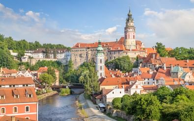 Middeleeuws kasteel met ronde toren kijkt uit over historische stad met rode pannendaken langs rivier in Český Krumlov.