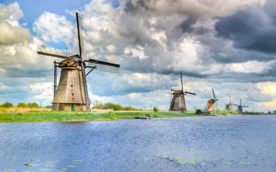 Rij traditionele Nederlandse molens van Kinderdijk UNESCO Werelderfgoed langs een waterweg onder dramatische bewolkte hemel.