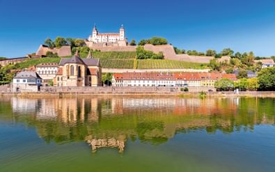 Festung Marienberg fort op een heuvel met wijngaarden in Würzburg, weerspiegeld in de Main. Kleurrijke gebouwen langs de waterkant.