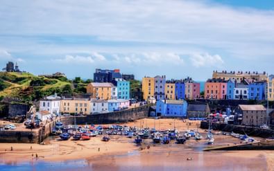 Kleurrijke Georgische huizen in roze, blauw, geel en wit langs de klif boven de haven van Tenby met boten op het strand bij eb.