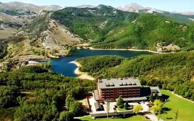 Luchtfoto van hotel Parador de Cervera in Palencia met een blauw meer en groene bergen. Het moderne gebouw is omgeven door gazons en bossen.