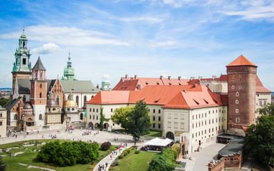Luchtfoto van het Wawel-kasteelcomplex in Krakau met rood gedekte gebouwen, kathedraal met groene koperen torens en ronde bakstenen toren.