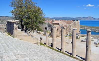 Antieke Griekse ruïnes in Lindos, Rhodos, met stenen zuilen en muren met blauwe Middellandse Zee op de achtergrond.