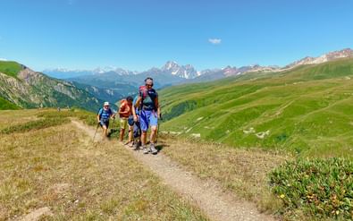 Groep wandelaars met rugzakken lopend op een bergpad in Georgië, omringd door groene heuvels en besneeuwde toppen onder blauwe hemel.