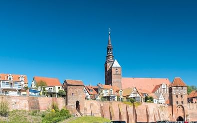 Middeleeuwse stad Tangermünde met rode bakstenen verdedigingsmuren, kerktoren met spits en traditionele Duitse huizen onder blauwe lucht.