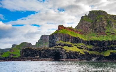 Dramatische basaltrotsen bedekt met groen gras die uit de zee oprijzen bij Carrick-a-Rede in County Antrim, Noord-Ierland, onder een bewolkte hemel.