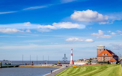 Rood-wit gestreepte vuurtoren bij de haven van Bremerhaven met historische bakstenen gebouwen, groen gazon en boten in het water onder blauwe lucht.
