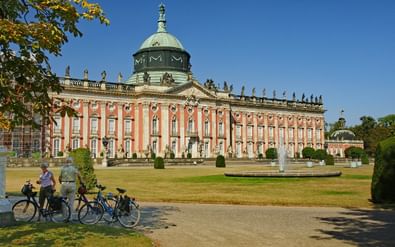 Fietsers met fietsen voor het barokke Neues Palais in Potsdam met zijn kenmerkende rode gevel en groene koperen koepel.