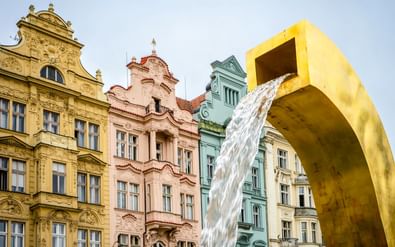 Grote gele moderne fonteinsculptuur met stromend water, voor kleurrijke historische gebouwen in Plzen, Tsjechië.