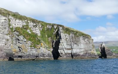 Dramatische kliffen bij Dingle Bay, Kerry Way Hoge kalksteenkliffen bij Dingle Bay langs de Kerry Way met diepblauw water eronder en groen landschap in de verte.