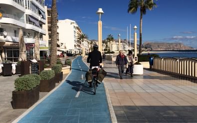 Fietser op boulevard van Altea Fietser op blauw betegeld fietspad langs Altea's boulevard met witte gebouwen, palmbomen en uitzicht op de Middellandse Zee.