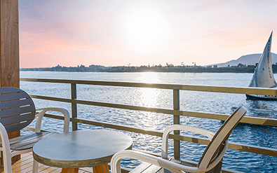 Uitzicht vanaf Nebu schip balkon in Egypte met witte stoelen en tafel met uitzicht op de Nijl met traditionele zeilboot en verre kustlijn.