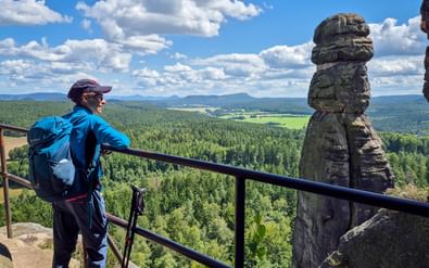 Wandelaar met rugzak en wandelstokken geniet van panoramisch uitzicht vanaf Pfaffenstein over bebost dallandschap.