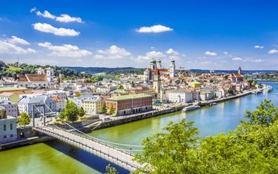 Panoramisch uitzicht op Passaus historische oude stad langs de Donau met kleurrijke gebouwen, kerktorens en een brug onder blauwe lucht.