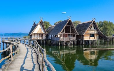 Historische paalwoningen in Unteruhldingen aan het Bodenmeer met houten loopbrug naar gereconstrueerde stelthuizen boven helder water.