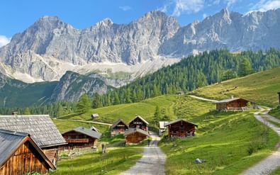 Traditionele houten berghutten verspreid over groene weiden in Ramsau met dramatische Dachstein-bergtoppen op de achtergrond.