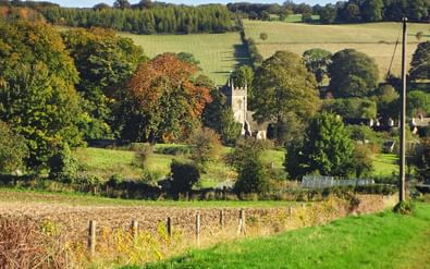 Blockley kerk in Cotswolds landschap Stenen kerktoren van Blockley omgeven door herfstbomen, groene velden en glooiende heuvels in het Engelse Cotswolds landschap.
