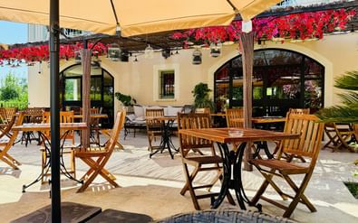 Buitenterras bij Ceres Boutique Hotel in Uzès met houten tafels en stoelen onder beige luifels. Rode bloemen sieren de witte gevelfacade.
