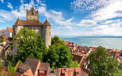 Middeleeuws kasteel Meersburg met ronde torens boven rood betegelde huizen, met uitzicht op het Bodenmeer met zeilboten.