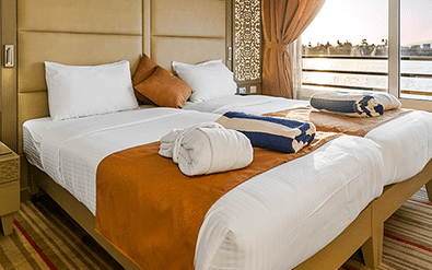 Moderne Nebu suite met twee bedden, wit beddengoed, oranje accenten en grote ramen met uitzicht op de Nijl in Egypte.