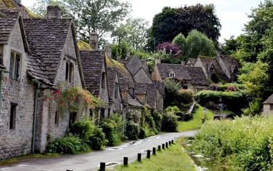 Pittoreske stenen huisjes met leien daken langs een bochtige weg in Castle Combe, Cotswolds. Een beekje stroomt ernaast met houten palen.