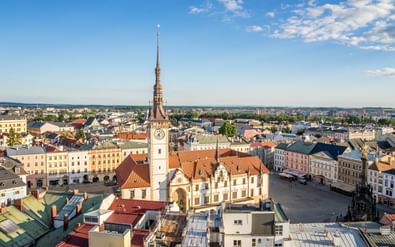 Luchtfoto van het stadsplein van Olomouc met wit stadhuis en hoge klokkentoren. Historische gebouwen met rode daken rondom het plein.