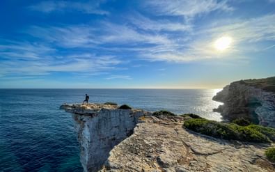 Eenzame wandelaar op dramatische witte kalksteenklif bij Ses Piquetes, Mallorca's oostkust, uitkijkend over turkooizen Middellandse Zee onder zonnige hemel.