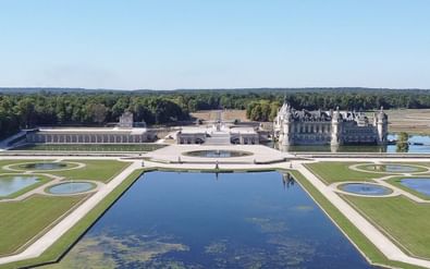 Luchtfoto van Kasteel van Chantilly met symmetrische Franse tuinen met een grote centrale vijver, geometrische waterpartijen en gemaaide gazons.