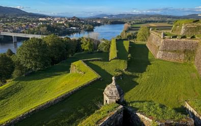 Luchtfoto van vesting Valença met stenen muren en wachttoren, uitkijkend over rivier met brug en stad op de achtergrond onder blauwe lucht.