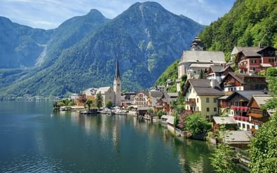 Hallstatt dorp met traditionele huizen en kerktoren aan de oever van een turquoise meer, omringd door groene beboste bergen.