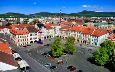Luchtfoto van het hoofdplein van Litoměřice met kleurrijke barokgebouwen, rode pannendaken, geparkeerde auto's en groene bomen.