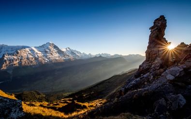 Dramatische zonsondergang in de Berner Alpen met zonnestralen die rechts achter een rotsachtige bergpiek schimmeren.