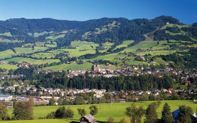Panoramisch uitzicht op Sankt Johann im Pongau in een groene alpenvallei met beboste bergen, traditionele gebouwen en kerktoren.
