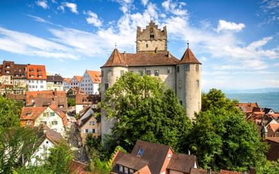 Middeleeuws kasteel Alte Burg in Meersburg met stenen torens en rode pannendaken, omringd door kleurrijke huizen en groene bomen met uitzicht op het Bodenmeer.