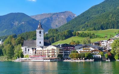 Schilderachtig uitzicht op St. Wolfgang dorp aan het Wolfgangsee met witte kerktoren, traditionele Oostenrijkse gebouwen en beboste bergen.