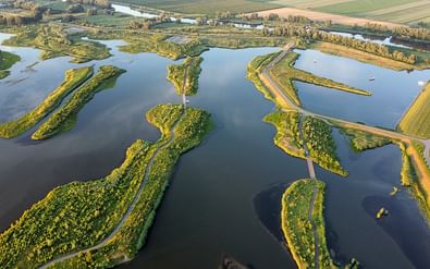 Luchtfoto van Nationaal Park de Biesbosch met groene beboste eilanden verbonden door wegen door blauwe waterwegen en wetlands.