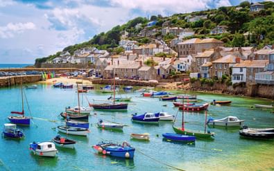 Kleurrijke vissersboten afgemeerd in de haven van Mousehole met turquoise water. Stenen huizen op de heuvel boven de haven in Cornwall.