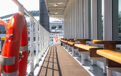 Overdekt promenadedek op MS Lisabelle met houten banken, witte relingen en reddingsboeien. Het dek heeft een gestructureerd looppad met zwarte lijnen.