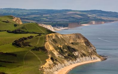 Golden Cap klif aan Dorsets Jurassic Coast met zandstrand eronder, groene heuvels erboven en kustgezichten in de verte.