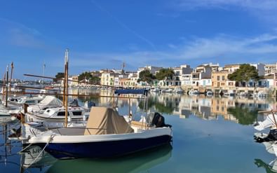 Rustige haven van Portocolom met vissersboten afgemeerd in kalm turquoise water, kleurrijke mediterrane gebouwen langs de waterkant.
