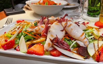 Kleurrijke zeevruchten salade met gegrilde inktvis, verse aardbeien, gemengde sla en groenten op wit bord in restaurant.