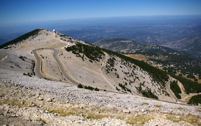 Luchtfoto van de kale top van Mont Ventoux met kronkelende weg door rotsachtig terrein. Observatorium zichtbaar op de top, Provence-vallei beneden.