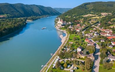 Luchtfoto van Schönbühel met kasteel aan de Donau in de Wachau, Oostenrijk. Groene heuvels, woonwijk en turquoise rivier zichtbaar.