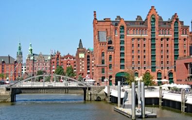 Rode bakstenen pakhuizen van Hamburg's Speicherstadt wijk langs een kanaal met boten aangemeerd aan houten steigers en een brug.