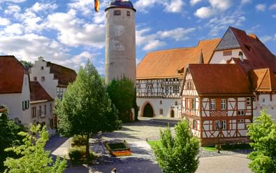 Kasteel Tauberbischofsheim met witte toren, oranje pannendaken, vakwerkhuizen en geplaveide binnenplaats onder blauwe hemel.