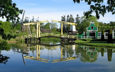 Gele houten ophaalbrug over kalm water in Nederlands Openluchtmuseum Arnhem, met traditioneel groen Nederlands huis en perfecte spiegeling.